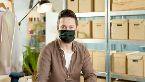 cucasian designer man wearing black facial mask and looking at camera in a good mood in a fashion clothing store