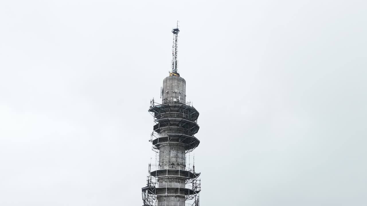 Aerial close up moving to a wide shot of a bleak industrial concrete television and radio link tower in Pasila, Helsinki, Finland on a bright and foggy day