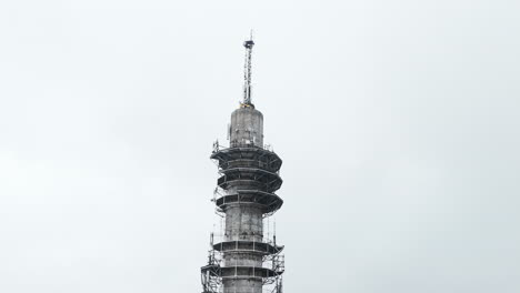 Aerial-close-up-moving-to-a-wide-shot-of-a-bleak-industrial-concrete-television-and-radio-link-tower-in-Pasila,-Helsinki,-Finland-on-a-bright-and-foggy-day