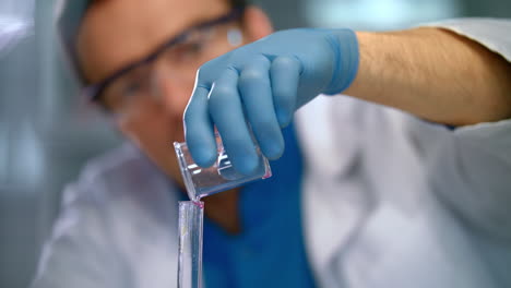 Scientist-pouring-liquid-in-glass-flask.-Close-up-of-chemist-in-medical-gloves