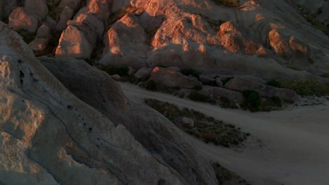 AERIAL:-Car-driving-on-a-dirt-road-in-middle-of-desert-rocks,-sunset-in-USA