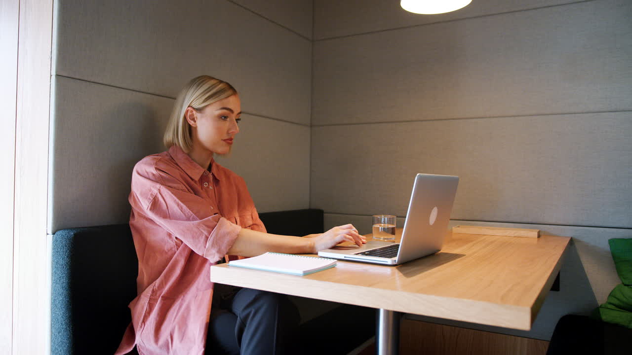 젊은 백인 여성이 사무실 식당의 부스 테이블에서 노트북에서 혼자 일하는 측면 시각, 을 확대합니다.