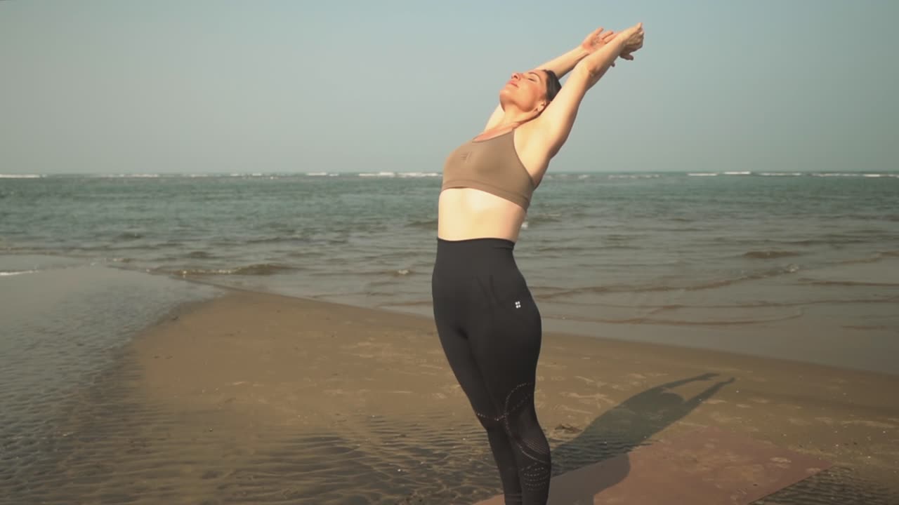 mujer de pie haciendo ejercicios de yoga en la orilla de una playa