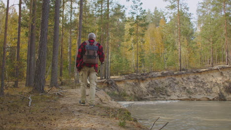 aged-fisherman-is-walking-over-coast-of-natural-forest-lake-carrying-spin-fishing-rod-back-view-of-man