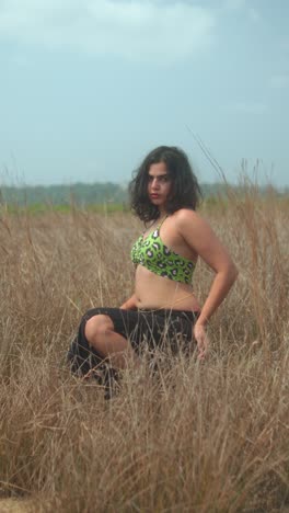woman posing confidently in dry grass field wearing green bikini top outdoors
