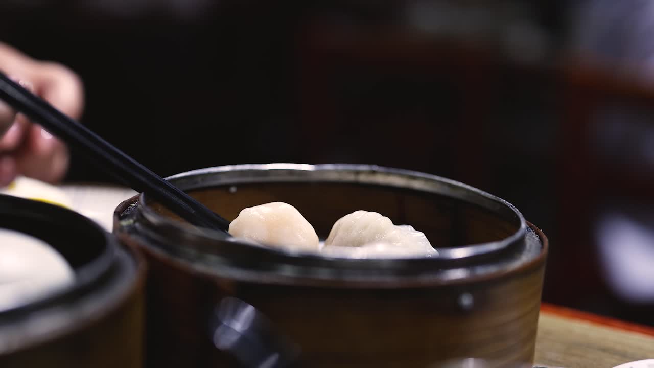 Chopsticks picking shrimp dumplings from a steamer