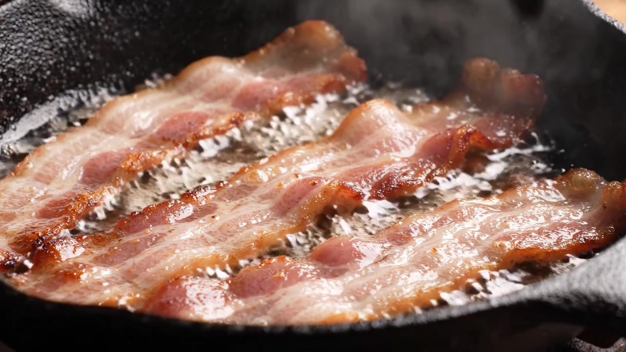Pancetta deliziosamente sfrigolante che cuoce in una padella di ghisa: strisce di pancetta perfettamente croccanti, saporite e dorate che friggono nel loro stesso grasso.