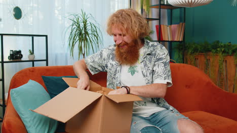 glücklicher rothaariger käufer, der kartonschachtel auspackt, paket liefert, online einkaufen, zu hause kauft