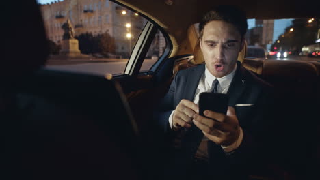 hombre de negocios molesto maldiciendo en el chat de video en el teléfono inteligente en un coche oscuro.