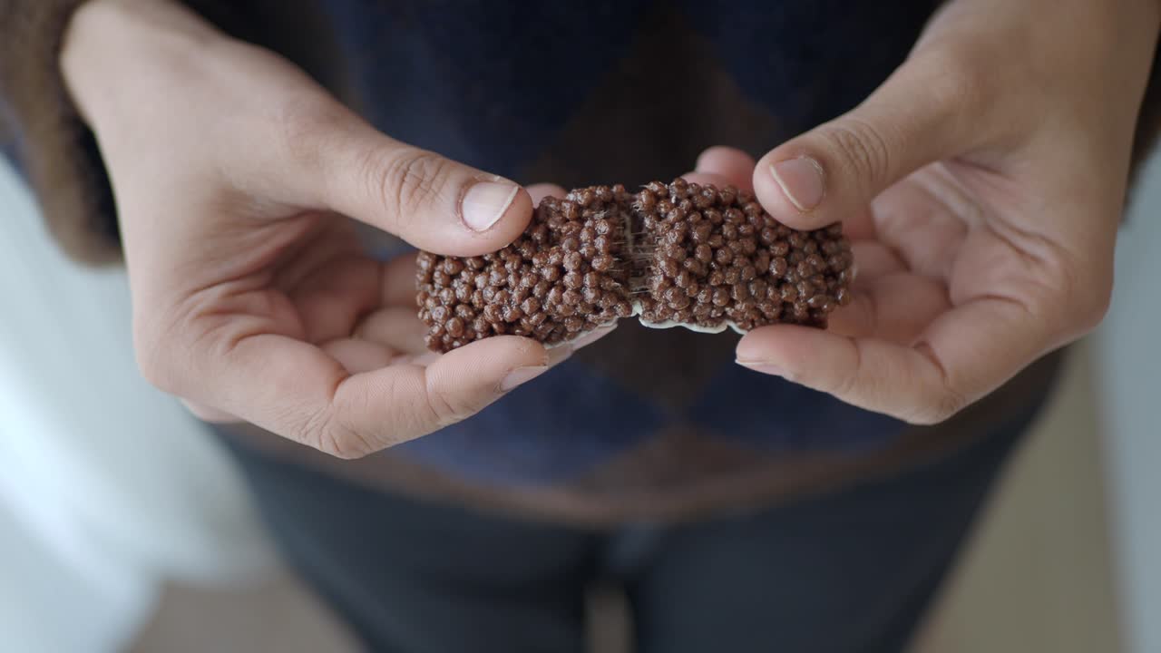 Primo piano di mani che spezzano una barretta di riso soffiato al cioccolato.