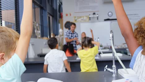 Rear-view-of-mixed-race-schoolkids-raising-hands-in-the-classroom-4k