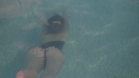 una mujer joven nada bajo el agua alejándose de la cámara, luego sale del agua y gira
