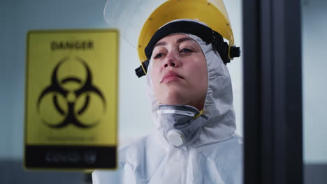A healthcare worker or scientist in a hazmat suit and face shield with a distressed expression, next to a 'Danger Biohazard COVID-19' sign