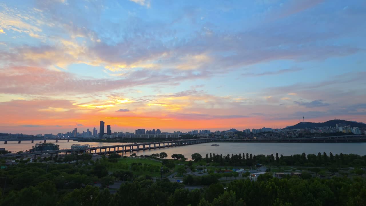 Seoul cityscape at dusk featuring vibrant sunset sky, Banpo Bridge over Han river and Namsan Tower with green Hangang Park