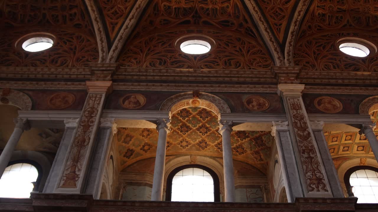 Panoramica verso l'alto del soffitto ornato di una chiesa con affreschi e archi.