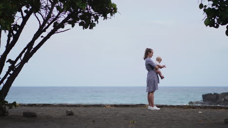 amidst the beauty of the sea and beach, a touching portrait showcases a mother kissing her daughter's cheek. a vacationing family shares moments of joy, and the mom lovingly hugs her toddler