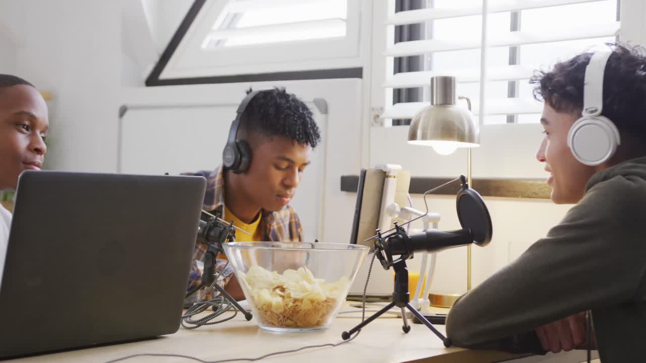 Happy diverse male teenage friends using laptop and recording podcast, slow motion
