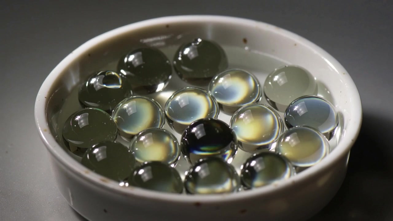 Showing beads shifting rings in white dish with clear liquid on dark table as light shifts