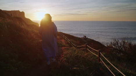 woman hiking on a cliff path at sunset