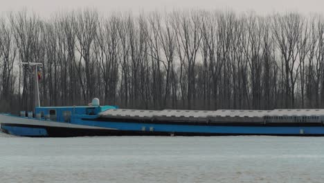 Close-up-shot-of-a-blue-transportation-river-barge,-Danube,-trees-in-the-background