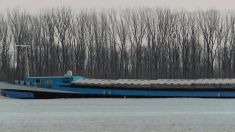 close up shot of a blue transportation river barge, danube, trees in the background