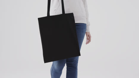 caucasian woman wearing white hoodie holding black bag on white background, copy space, slow motion