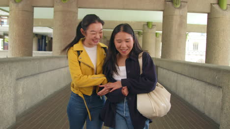 Front-View-Of-Two-Young-Female-Friends-Walking-Through-The-Barbican-Centre-In-City-Of-London-Together