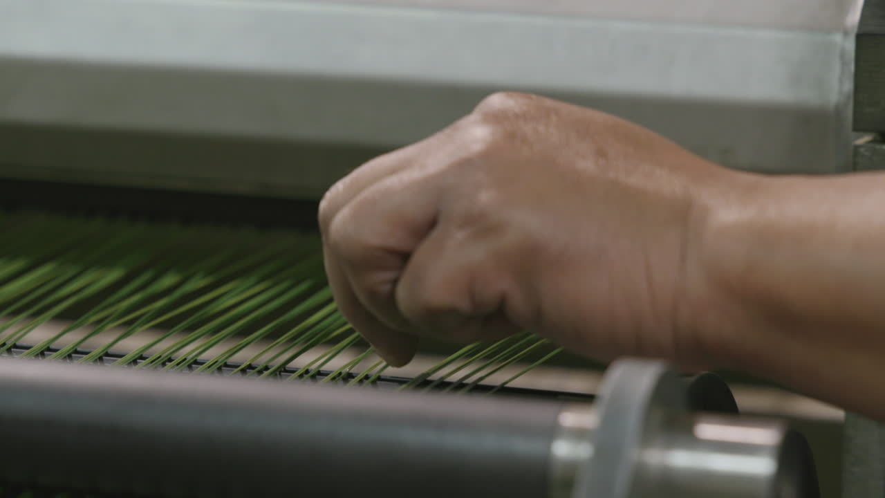 Close up footage of a hand and fingers working on thread that is moving through a machine