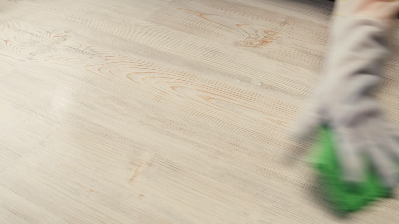 Gloved Hand Spraying and Wiping a Wooden Surface