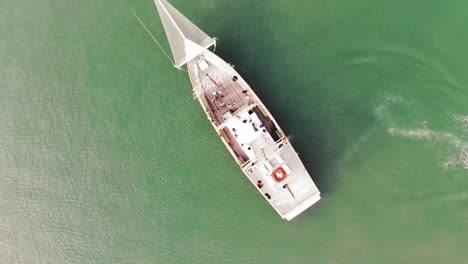 Aerial-top-down-of-gigantic-sailing-boat-cruising-on-transparent-green-water-in-summer