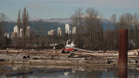 Piles-of-Floating-Logs-with-Tug-Boat-Passing-Through-and-City-in-the-Background