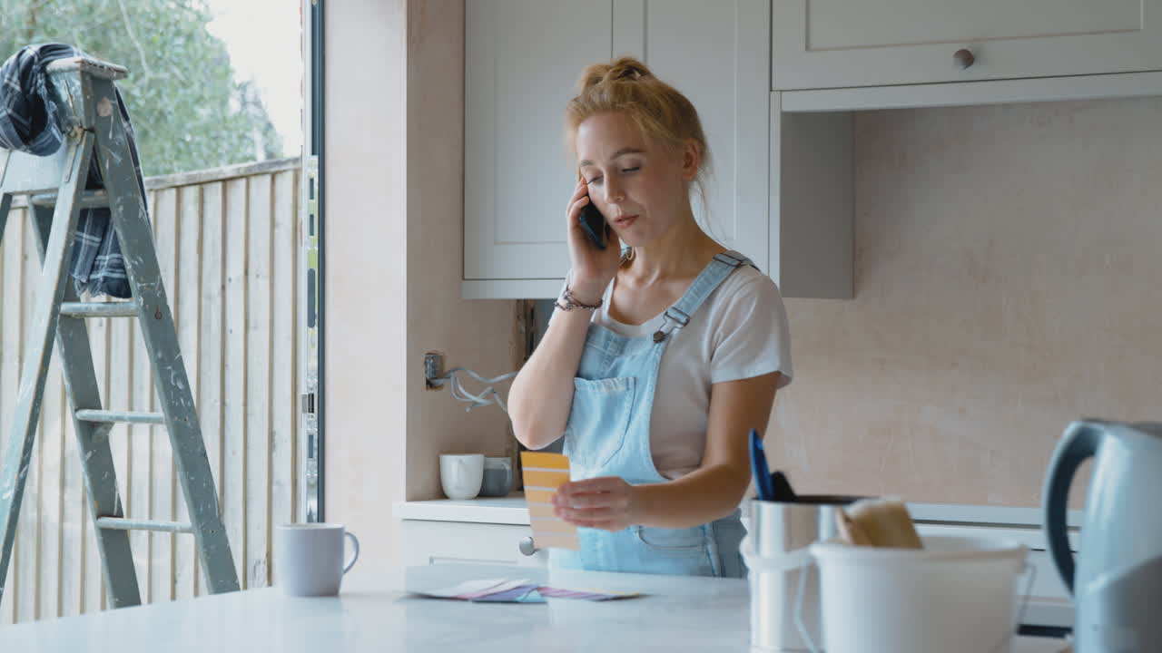 Kvinde renoverer køkken derhjemme, kigger på farveprøver og taler i mobiltelefon.