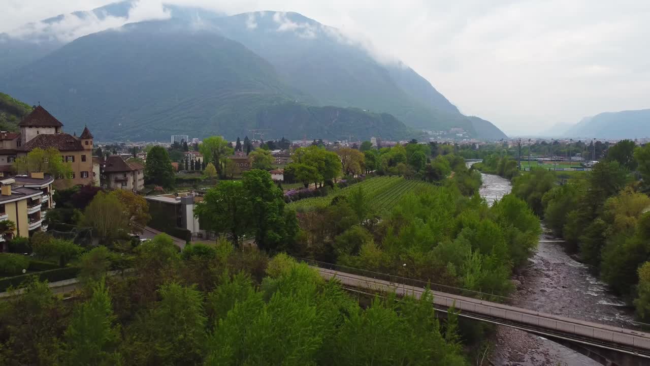 Misty Mountain Valley with River, Bridge, and Castle Overlooking Forested Town Under Overcast Sky