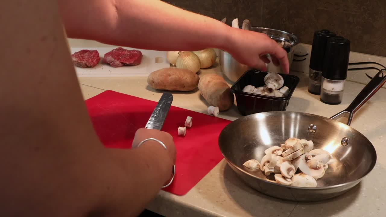 Mulher fatiando cogumelos-de-paris usando uma faca de chef japonesa e uma tábua de corte vermelha.