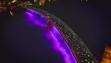 Vista-Aérea-Del-Puente-Starlight-O-Del-Puente-Anh-Sao-Por-La-Noche,-Un-Puente-Peatonal-Con-Luces-De-Colores-Fuertes-Y-Cascada-En-El-Distrito-7-De-La-Ciudad-De-Ho-Chi-Minh,-Vietnam