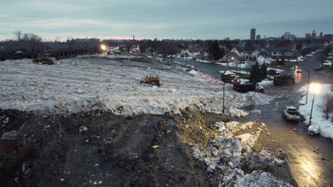 Toma-Nocturna-Aérea-De-Camiones-Que-Descargan-El-Exceso-De-Nieve-En-El-Sitio-De-Almacenamiento-En-Buffalo,-Nueva-York