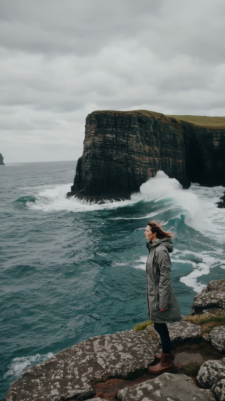 Woman on a rugged cliff overlooking the stormy Atlantic Ocean in the Faroe Islands