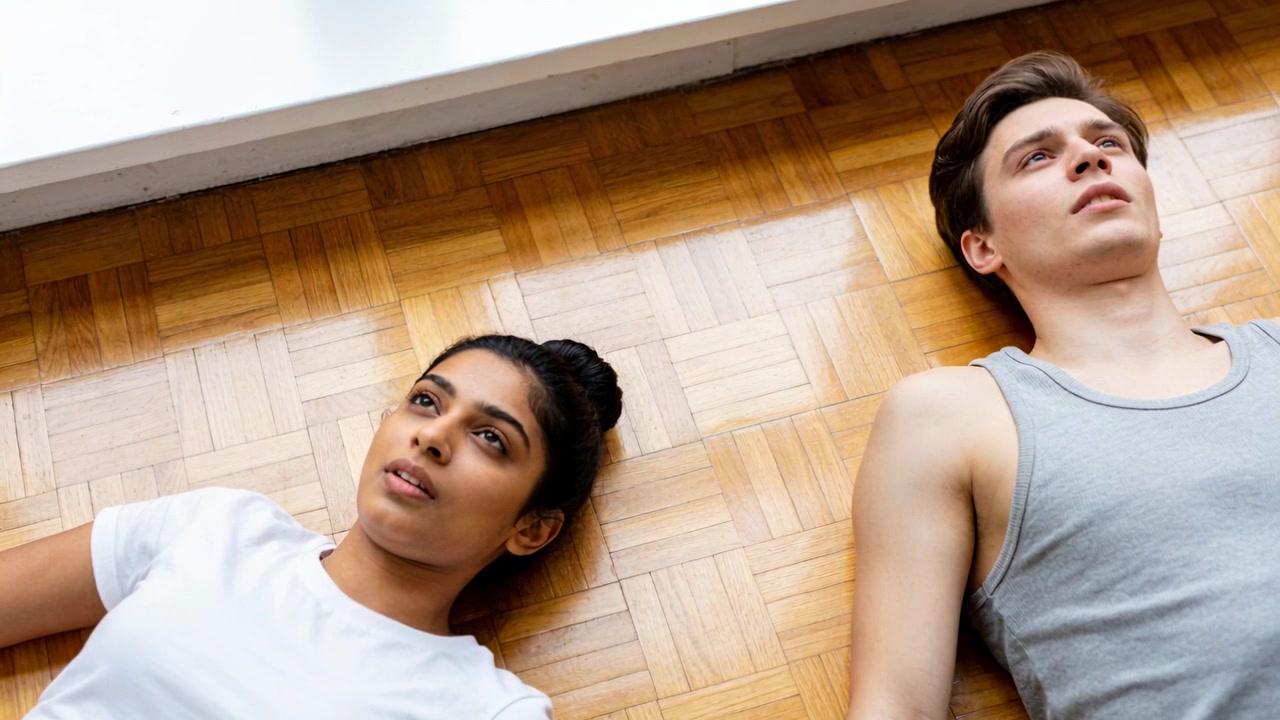 Exhaling man, blinking woman lying on parquet floor near white baseboard, in white tee gray tank