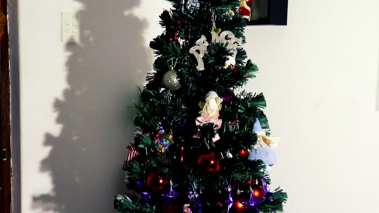 Camera tilting down onto a decorated Christmas tree with father Christmas snowmen and magic Elfes figurines laying underneath the tree