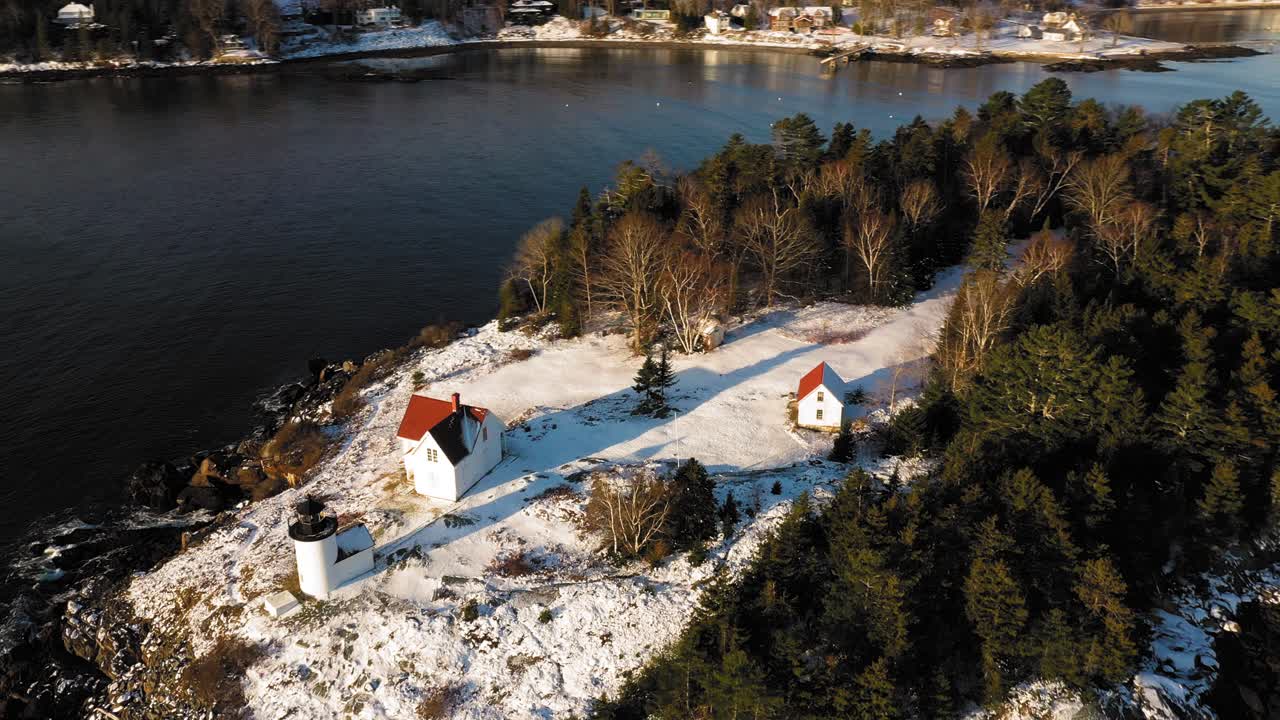 눈 속에 긴 그림자가 있는 일출의 눈 덮힌 커티스 섬 등대 위의 공중 궤도
