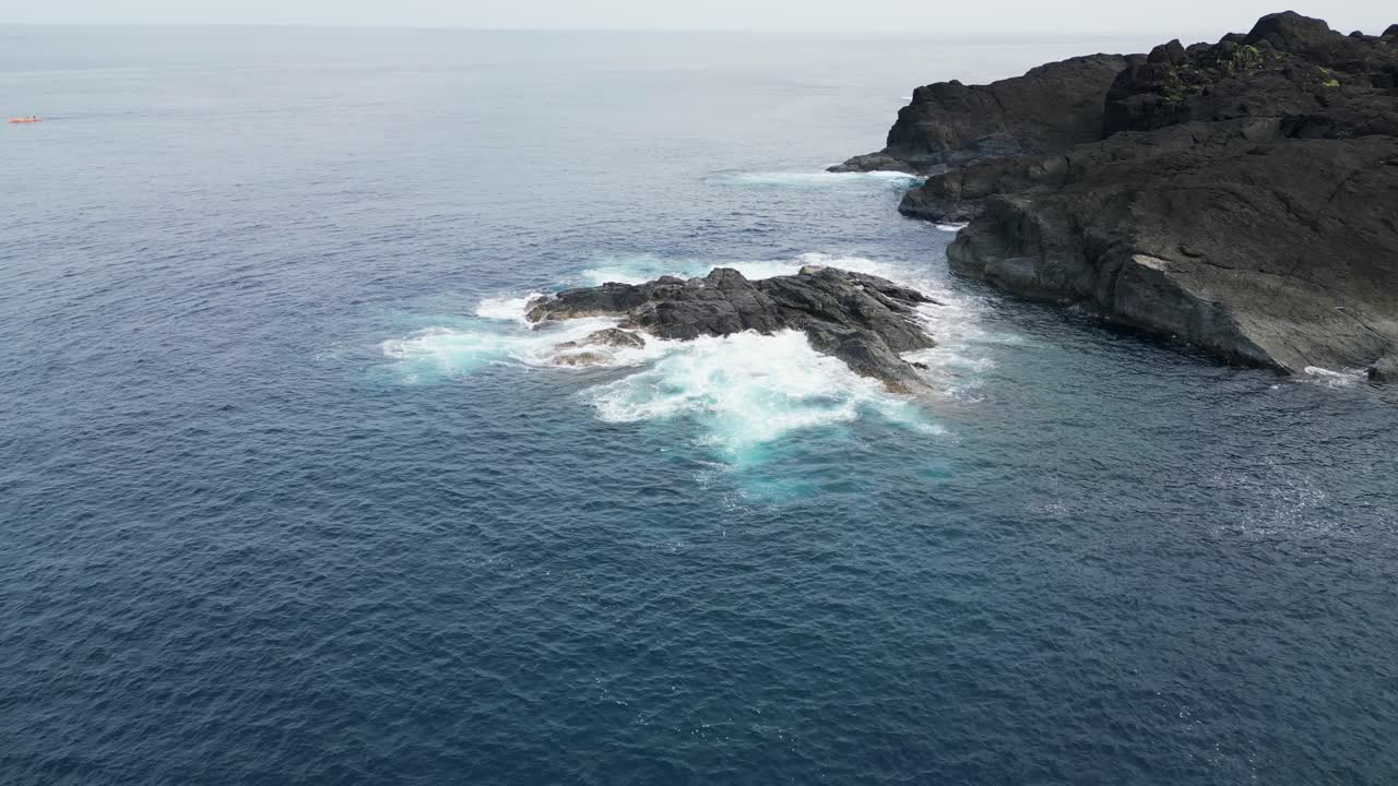 Flyover drone shot of idyllic ocean waves crashing against sharp rocks facing the tropical island of Catanduanes, Philippines