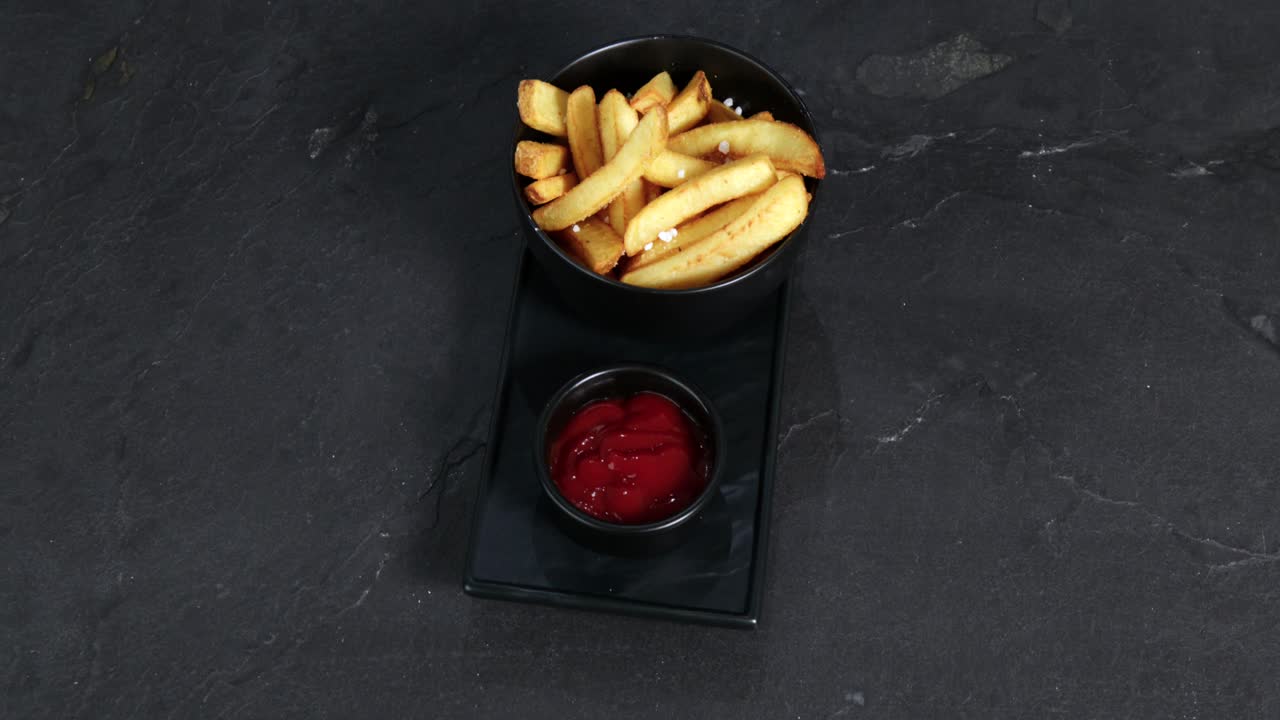 Patatine fritte con sale accanto a una tazza di ketchup sono presentate su un piatto girevole