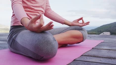 sección baja de mujer caucásica meditando en posición de loto en la cubierta en la ladera de la montaña rural