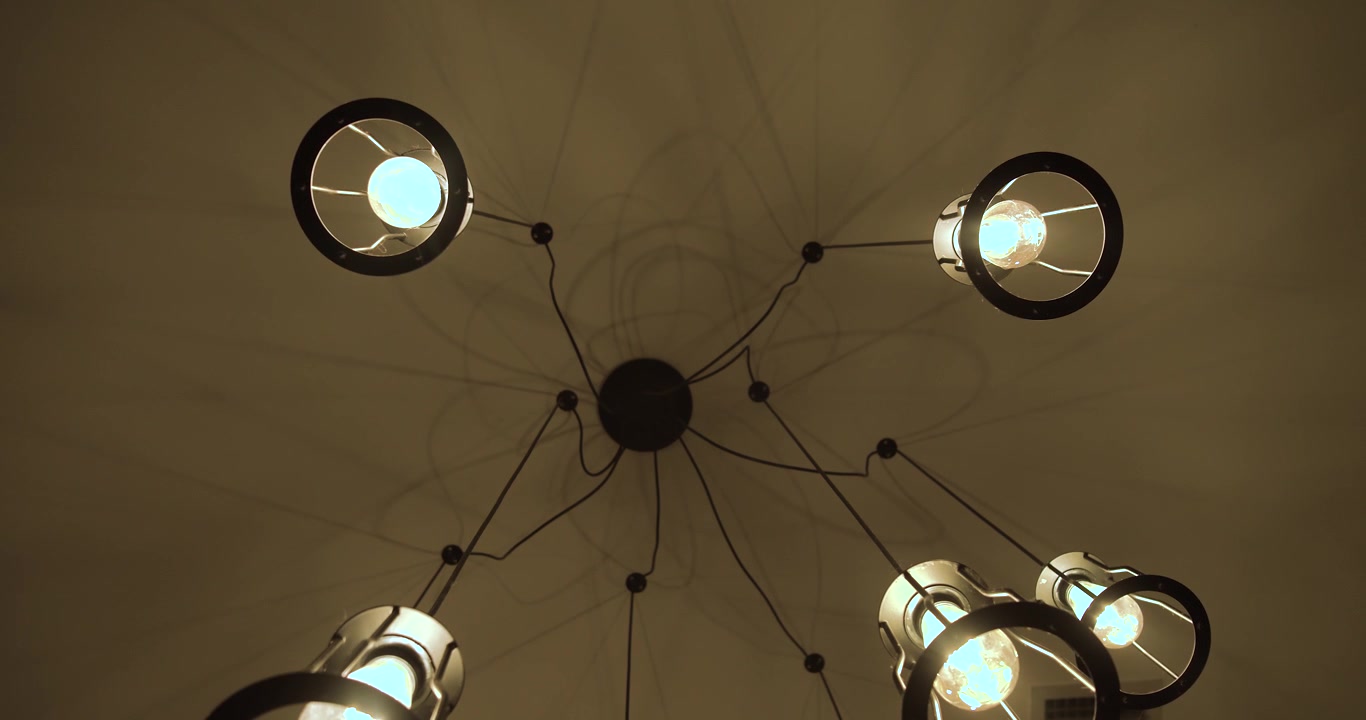 Una moderna luminaria de techo industrial con bombillas expuestas y brillantes. Acercamiento lento y sutil hacia el techo
