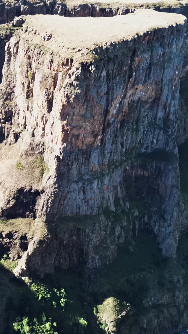 Aerial drone view of steep canyon cliffs surrounding Maletsunyane Falls in Lesotho, highlighting the dramatic rock formations and deep valley below. Vertical