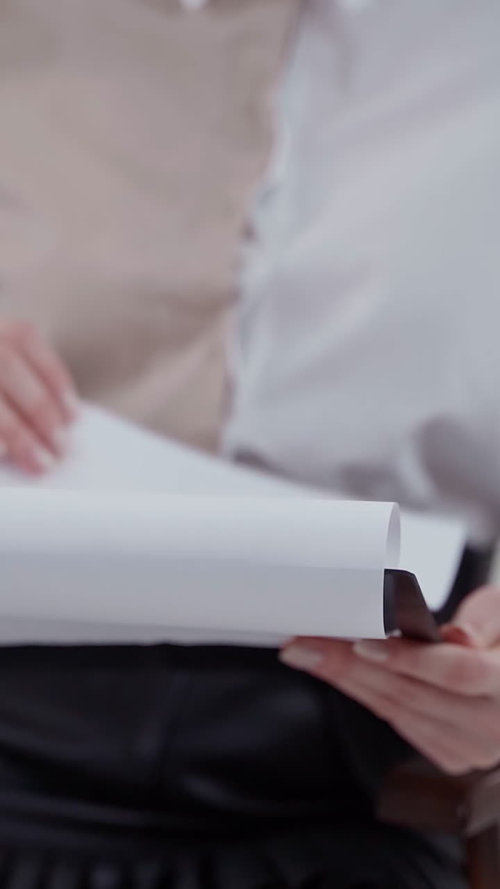 Folder in woman's hands. Young secretary in blouse sitting in the chair and flipping papers. Close-up. Slow motion. Vertical video