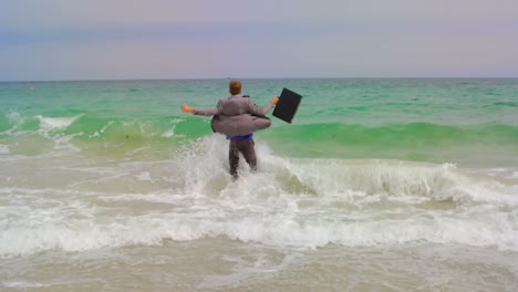 Rückansicht-Eines-Kaukasischen-Geschäftsmannes,-Der-Mit-Aktentasche-Im-Meer-Am-Strand-Läuft,-4k