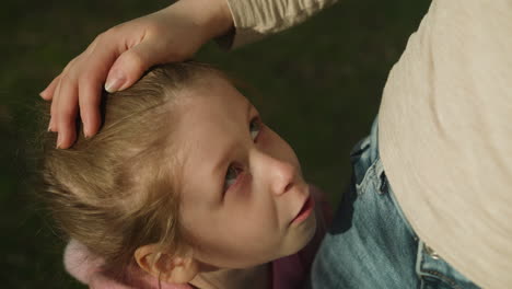 Mother-strokes-head-of-upset-little-girl-standing-in-park