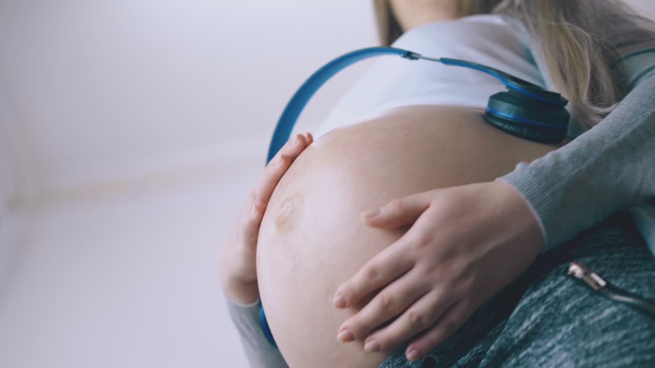 una bella donna incinta si rilassa con le cuffie in primo piano sulla pancia.