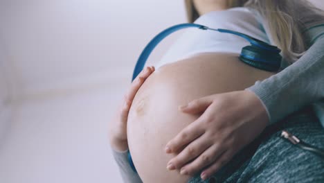 buena mujer embarazada se relaja con auriculares en primer plano del vientre